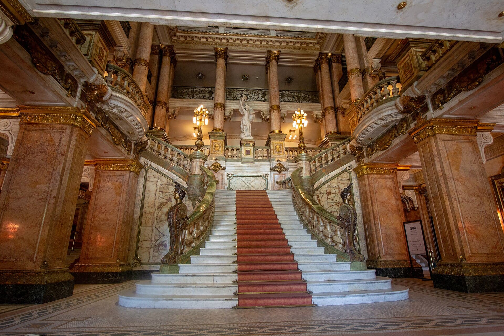 Grande escadaria de mármore com tapete vermelho no saguão do Theatro Municipal